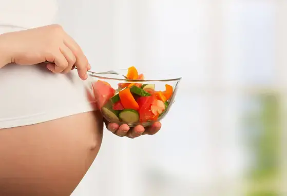 Mujer embarazada con un plato de verduras para hacer ensaladas.