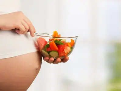 Mujer embarazada con un plato de verduras para hacer ensaladas. 